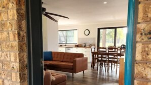 A modern living room with a brown sofa, a coffee table, and a dining area with wooden chairs and a table.