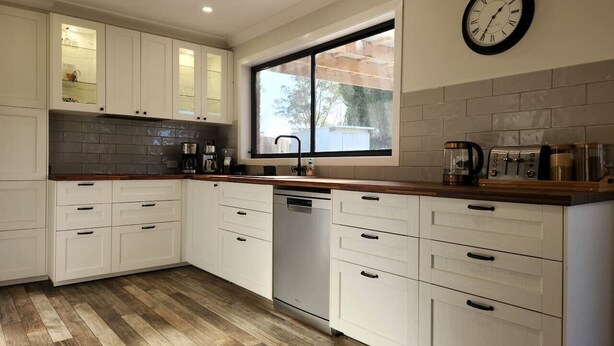 A kitchen with white cabinets, a dishwasher, a window, and a clock on the wall.