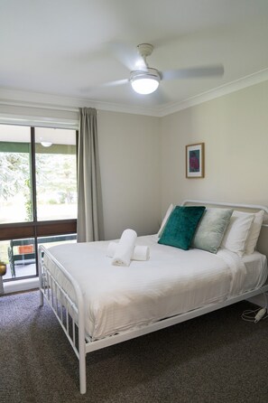 Ein Schlafzimmer mit einem Bett, einem Deckenventilator, einem Fenster mit Vorhängen und einem Bild an der Wand.