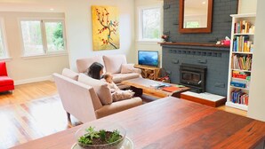A living room with a sofa, a coffee table, a fireplace, a bookshelf, and a TV. - BlackheathCottage|Cosy Woodfire|Quiet|Walks (Blackheath)