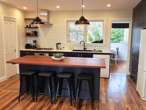 A modern kitchen with a central island, bar stools, pendant lighting, and a view of the outdoors.