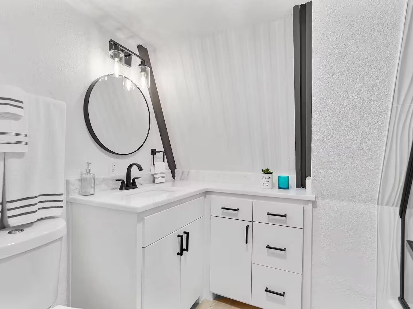 Un baño moderno con tocador blanco, espejo redondo, grifo negro y toallero.