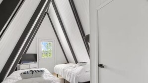Et soveværelse med skrå vægge, en seng, et skrivebord og en dør.