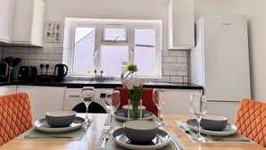 Una cocina moderna con armarios blancos, encimera negra y un comedor con sillas anaranjadas y una mesa dispuesta para cuatro.