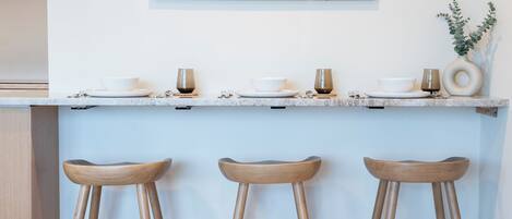 A modern kitchen with a light blue countertop, three wooden stools, and a framed artwork on the wall.