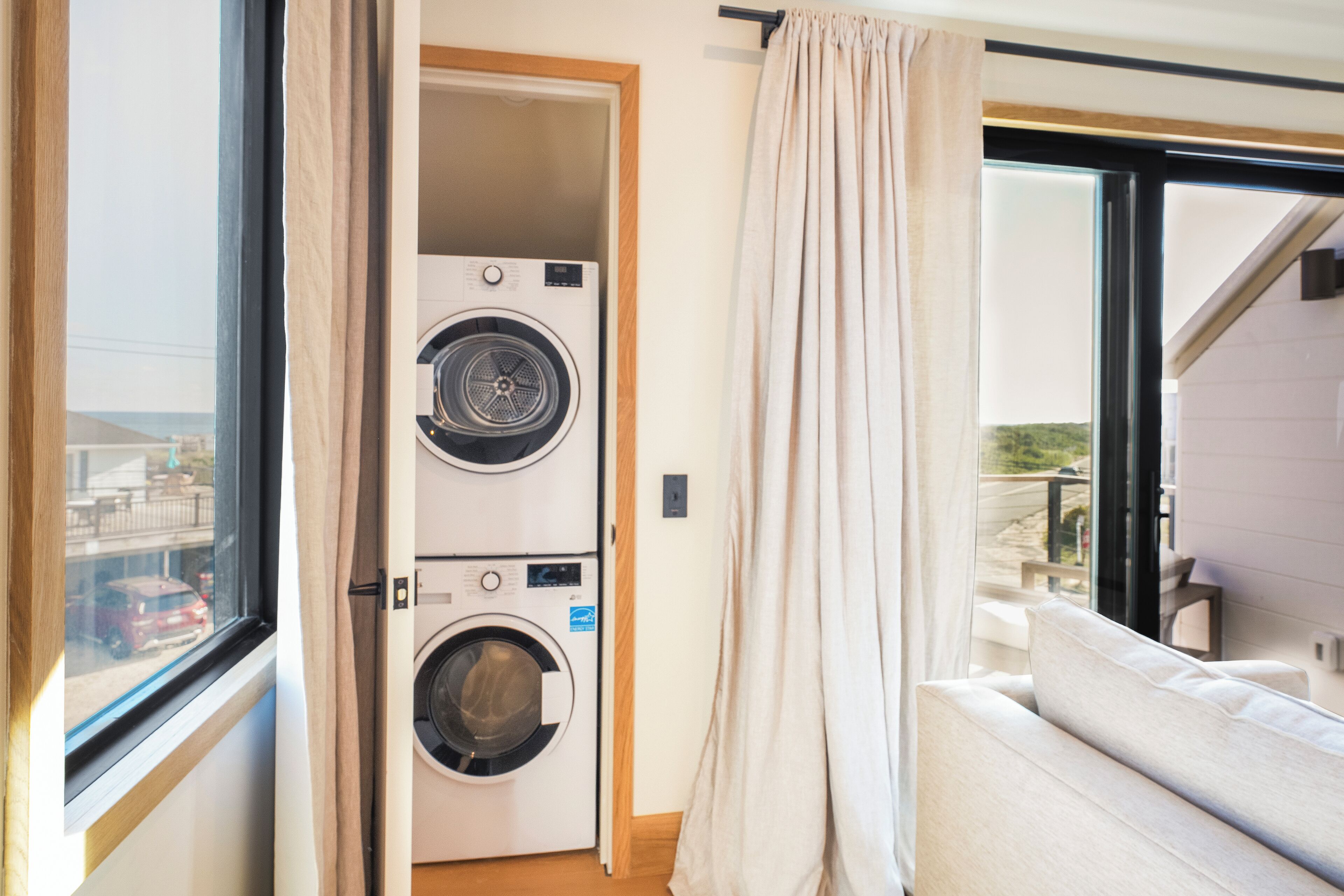 Un lavadero con dos lavadoras apiladas, una ventana con cortinas y vistas al exterior.