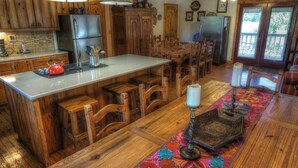A spacious kitchen with wooden cabinetry, a central island, and a dining area with wooden chairs and a table. - 4-bedroom house in Utopia with 450’ of private crystal clear Sabinal river front (Utopia)