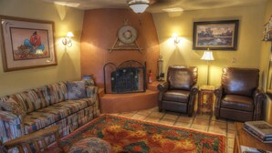 A living room with a patterned sofa, two leather armchairs, a decorative rug, a fireplace, wall-mounted lamps, and framed artwork. - 4-bedroom house in Utopia with 450’ of private crystal clear Sabinal river front (Utopia)