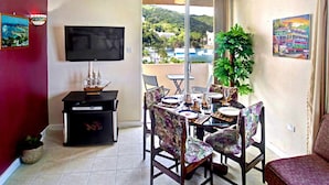 Un comedor con una mesa dispuesta para cuatro, un televisor en la pared y un balcón con vistas a una colina.