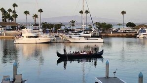A marina with boats docked, a gondola in the water, and palm trees in the background.