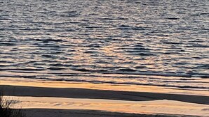 Un coucher de soleil sur l’océan, avec une plage au premier plan.