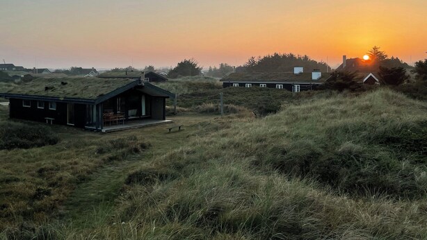 Un paysage rural avec deux maisons, l’une avec un toit vert et l’autre avec un toit blanc, se détachant sur le ciel d’un coucher de soleil.