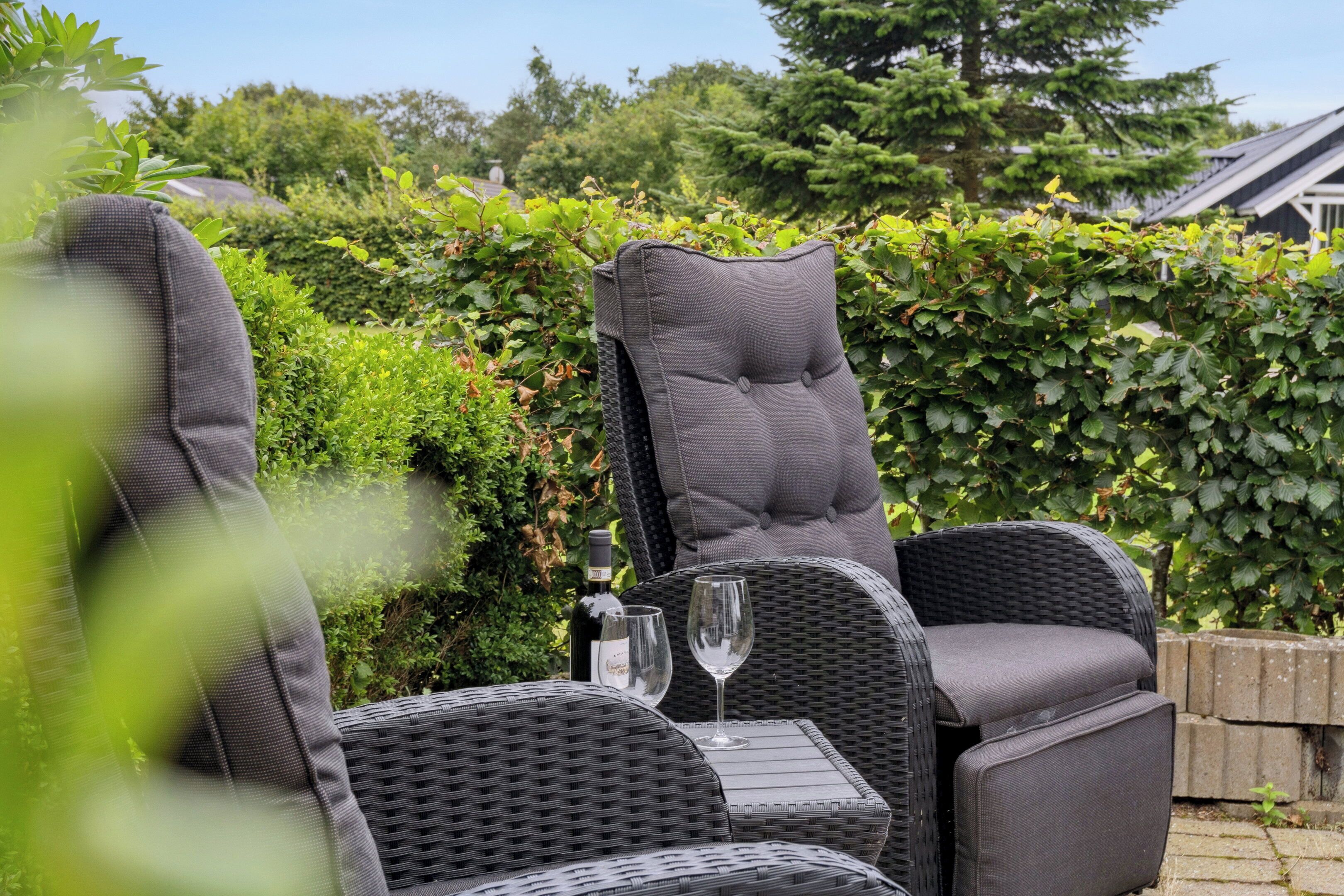 Mobilier d’extérieur en osier, agrémenté de coussins, un verre de vin et une bouteille de champagne.