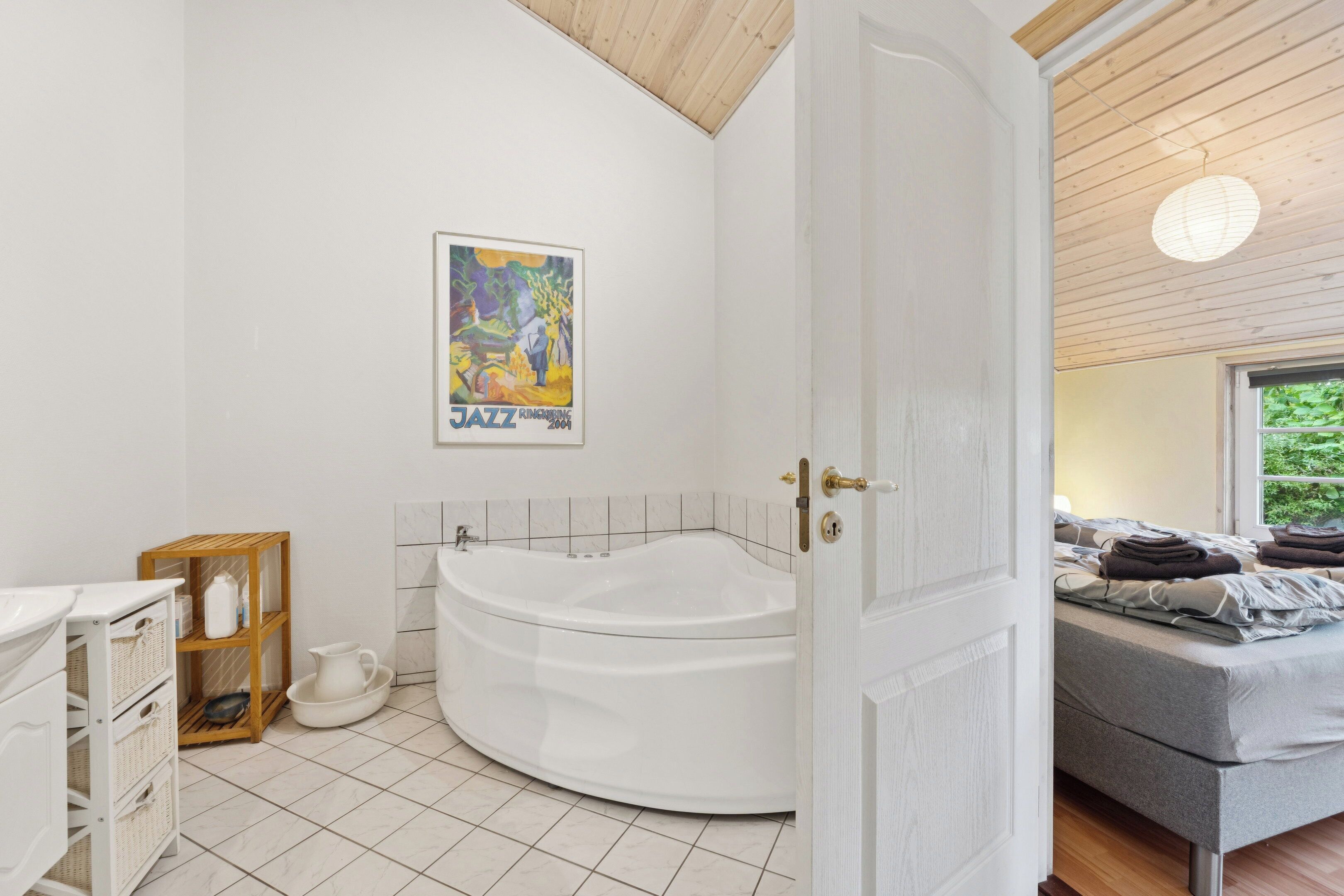 A modern bathroom with a freestanding bathtub, a wooden shelf with toiletries, and a poster on the wall.