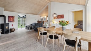 Un salon moderne avec un plafond en bois, une cheminée, un coin repas avec une table et des chaises en bois, et une grande fenêtre.