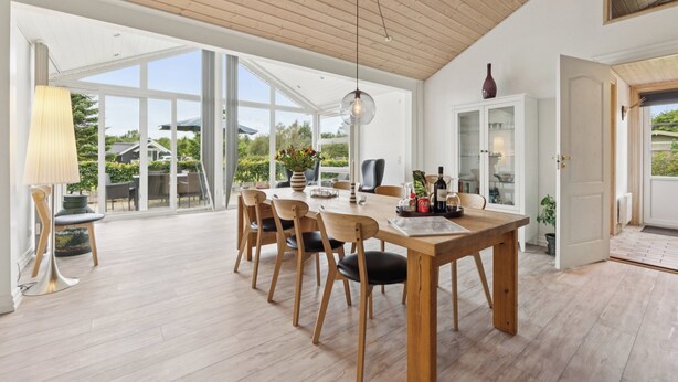 Un vaste espace dédié à la salle à manger, avec une table et des chaises en bois, de grandes fenêtres et une vue sur l’extérieur.