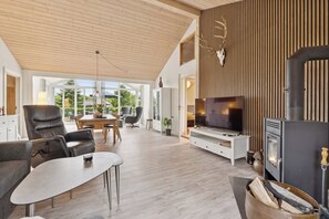 Moderni olohuone, jossa on takka, televisio ja ruokailutila, ja tila on valaistu luonnonvalolla.