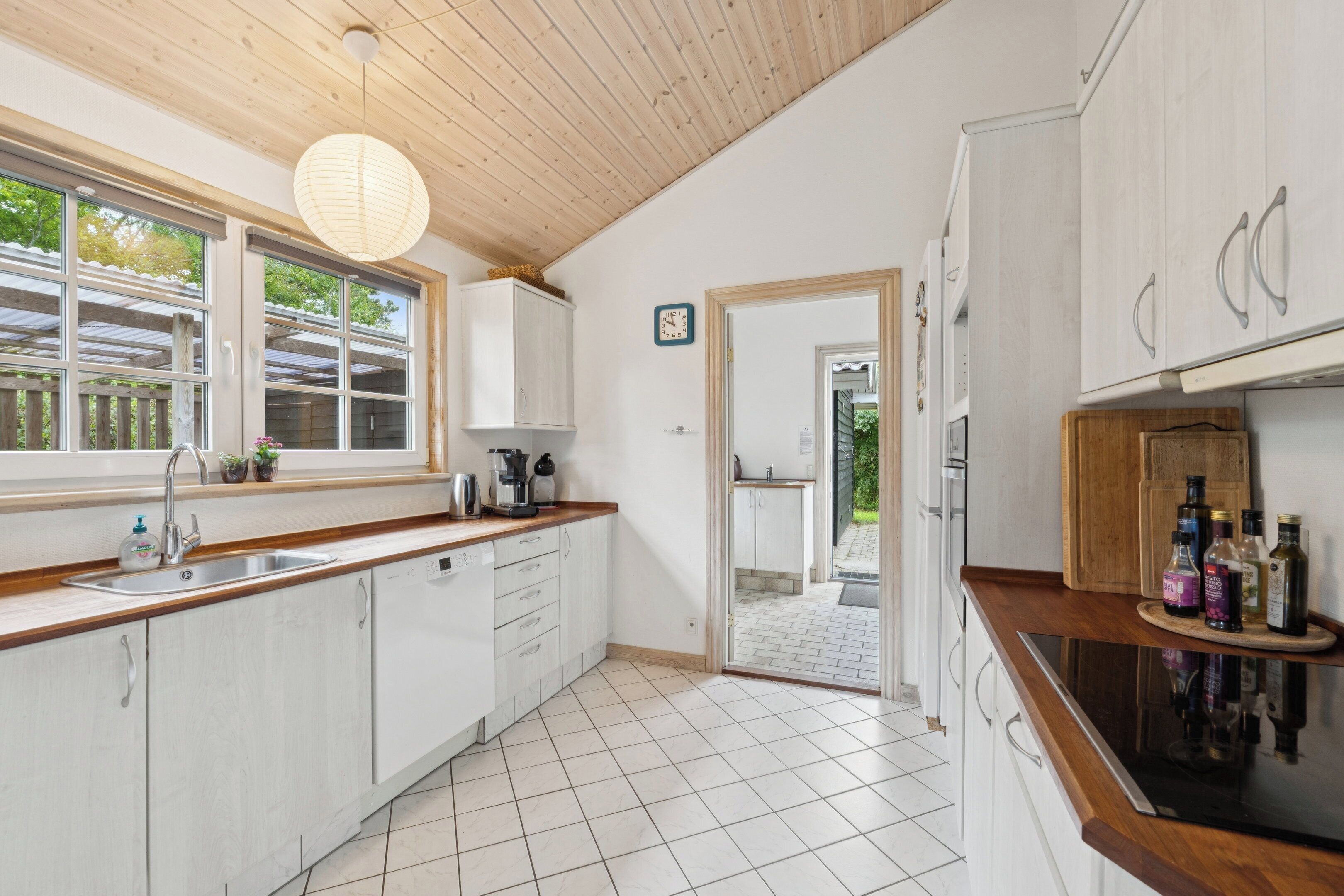 A kitchen with white cabinets, a wooden countertop, a sink, a hanging light fixture, and a door leading to an outdoor area.