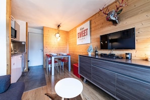 Eine moderne Küche mit Holzwänden, einem Essbereich mit roten Stühlen, einem runden weißen Tisch und einem dunklen Holzschrank mit Flachbildfernseher.