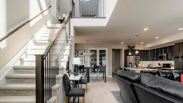 Un appartement moderne doté d’un escalier, d’un coin repas, d’un salon avec un canapé en cuir noir et d’une cuisine avec des meubles sombres et des appareils électroménagers en acier inoxydable.