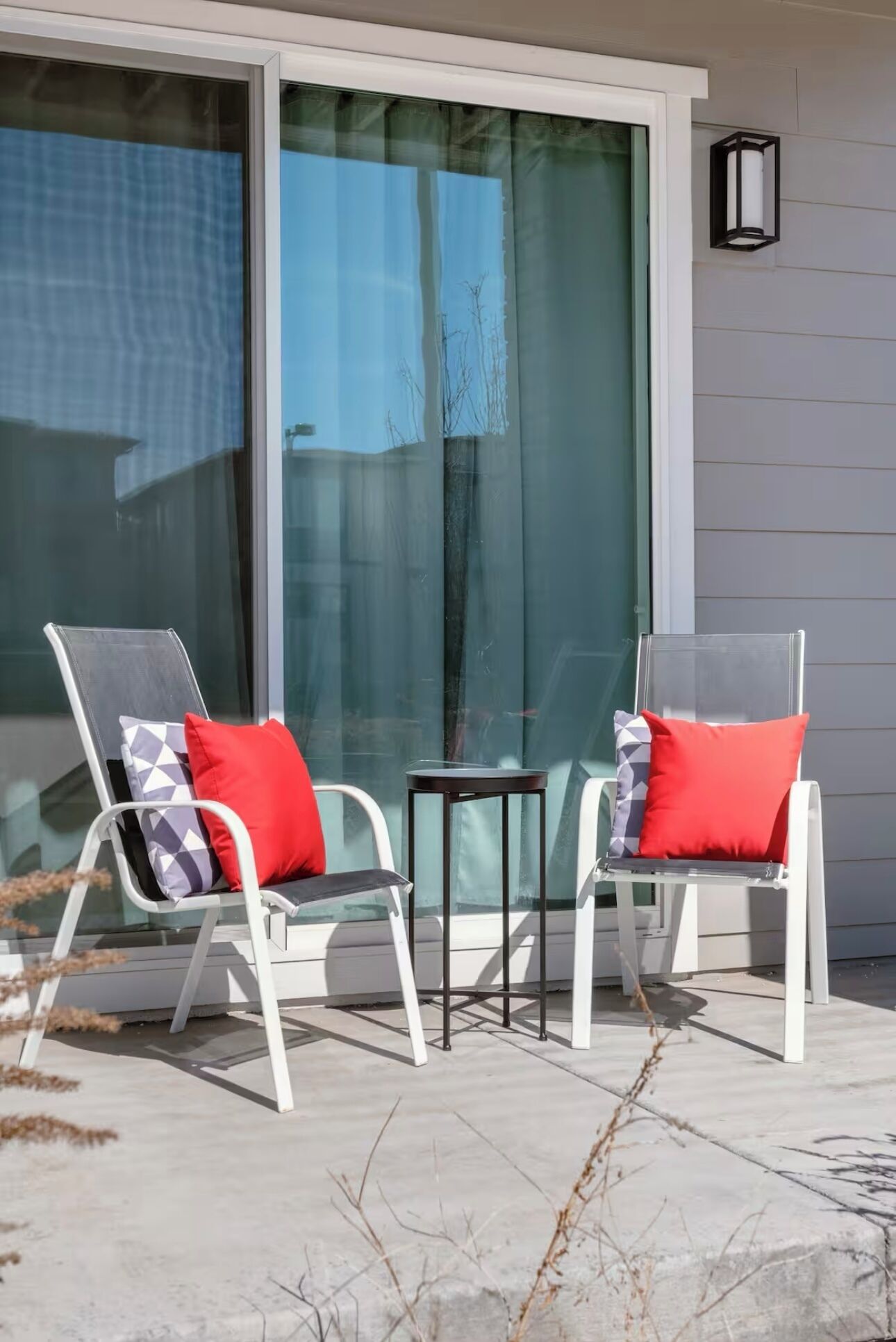 Two outdoor chairs with red cushions, a small table, and a glass door with a view of a building.