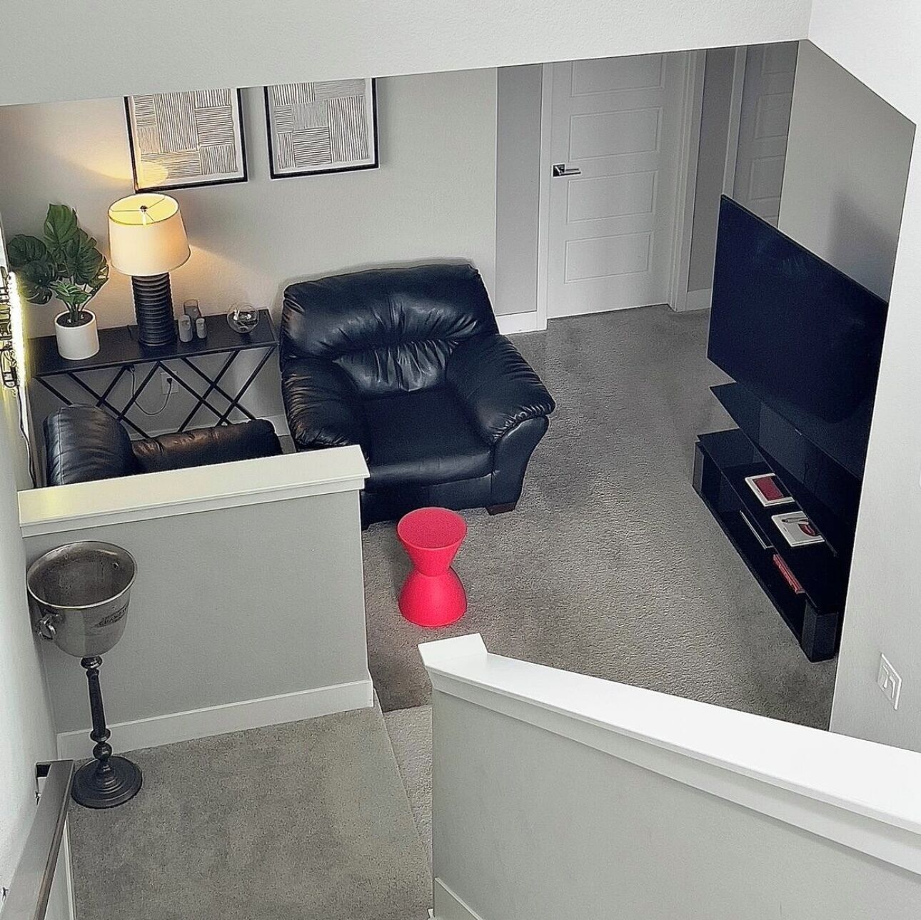 Een woonkamer met een zwarte lederen fauteuil, een rode kruk, een tv-meubel en lijstwerken aan de muur.