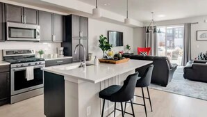 Une cuisine moderne dotée d’appareils électroménagers en acier inoxydable, d’un îlot central avec des tabourets de bar et d’un coin repas comprenant un canapé noir et des coussins rouges.