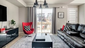 Un salon moderne avec un canapé en cuir noir, un fauteuil rouge, une table basse noire et un téléviseur placé à gauche.