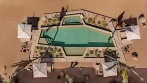 An aerial view of a resort with a central swimming pool, surrounded by lounge areas and palm trees. - WAMA Boutique Hotel - Depa Turrell (Todos Santos)