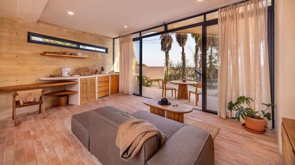 A modern living room with a sofa, a dining table, and a kitchen area. - WAMA Boutique Hotel - Depa Turrell (Todos Santos)