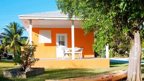 Un bâtiment d’un orange vif, doté d’un porche blanc, avec un kayak et un petit arbre à proximité.