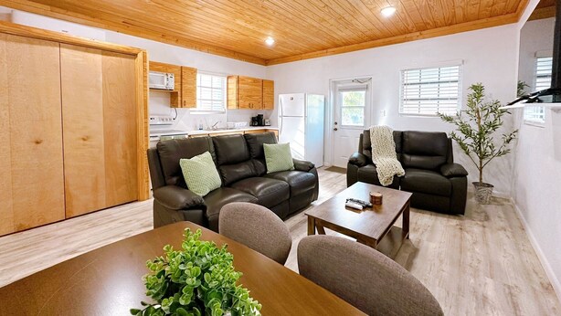 Un vaste espace de vie doté d’un plafond en bois, une cuisine à l’arrière-plan et une table à manger avec des chaises.