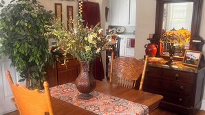 Un coin repas avec une table en bois, des chaises, un vase de fleurs, un tapis à motifs et un miroir au-dessus de la table.