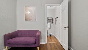 Un couloir avec un fauteuil violet, une œuvre d’art encadrée accrochée au mur, une porte blanche et une petite poubelle.