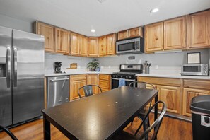 A modern kitchen with wooden cabinets, stainless steel appliances, and a dining table.