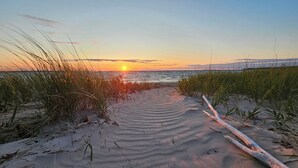 Ein Strandweg aus Sand und Gras, der zum Meer bei Sonnenuntergang führt.