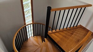 Eine Wendeltreppe mit Holzboden und schwarzen Geländern, die zu einer Zwischenebene mit einem Holzgeländer und einer hängenden Leuchte führt.