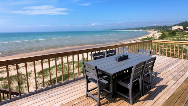 Eine Holzterrasse mit Tisch und Stühlen mit Blick auf Strand und Meer.