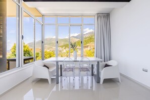 A modern dining area with a large table, clear chairs, and a view of mountains and greenery.