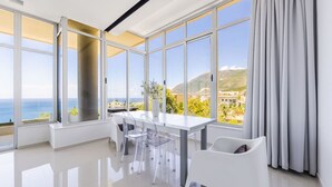 Ein modernes Zimmer mit großen Fenstern, einem weißen Tisch und klaren Stühlen.