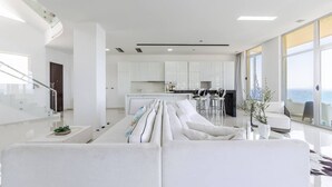 Ein modernes Wohnzimmer mit einer Couch, einem Essbereich mit Barhocker und einer Küche mit weißen Schränken.