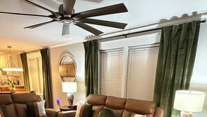 A living room with a brown leather sofa, a round coffee table, and a ceiling fan. - Relax at Cricket & Clover Retreat Near SU, LSU, Airport, Downtown, WiFi & AC (Baton Rouge)
