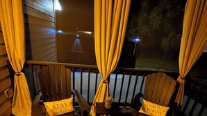 A deck with two wooden chairs, each with a cushion labeled "STAY awhile." A small table with a pineapple and a bottle is between the chairs. - Relax at Cricket & Clover Retreat Near SU, LSU, Airport, Downtown, WiFi & AC (Baton Rouge)