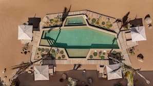 Vue aérienne d’un complexe hôtelier doté d’une piscine centrale, entourée d’espaces de détente et de palmiers.