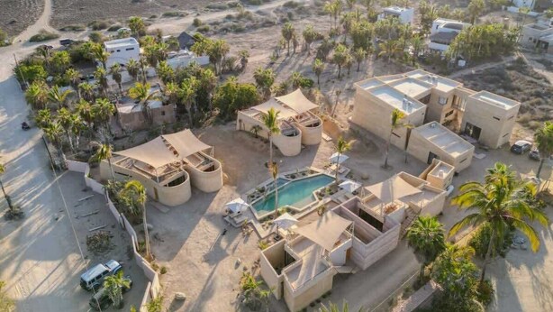 Vue aérienne d’un complexe hôtelier comprenant plusieurs bâtiments, une piscine et des palmiers.