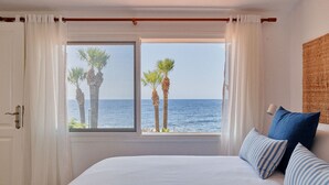 A bedroom with a large bed, a view of the sea, and palm trees outside the window. - Bright oceanfront bungalow with views, garden and coastal style, 91 (San Miguel de Abona)