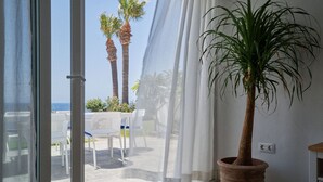 A room with a large window, a potted plant, and a view of palm trees and a patio area. - Bright oceanfront bungalow with views, garden and coastal style, 91 (San Miguel de Abona)