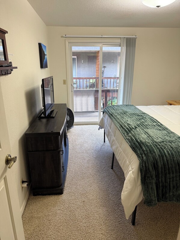 A hotel room with a bed, a desk with a computer, a window with a view of the outside, and a door.