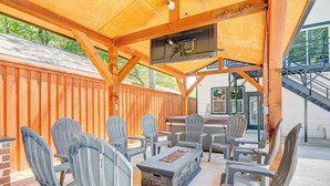 An outdoor patio with wooden beams, a stone fire pit, and several Adirondack chairs.