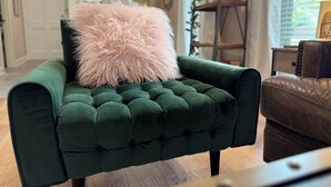 En grøn, polstret lænestol med en blød, lyserød pude, placeret i et rum med trægulv og en brun lædersofa.